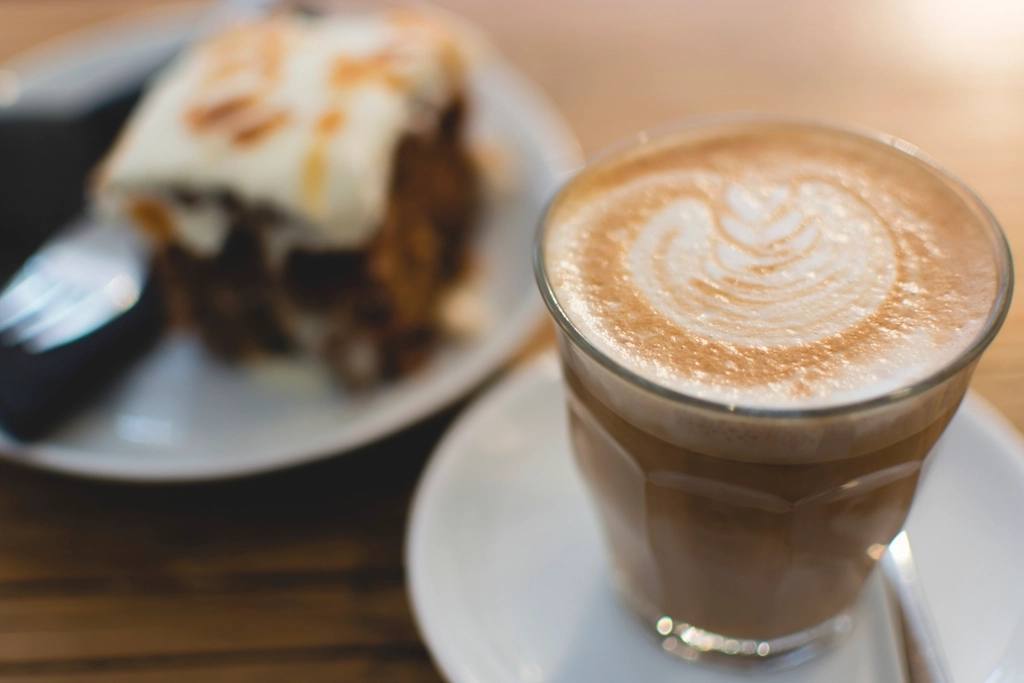 A cappuccino with latte art beside a slice of cake